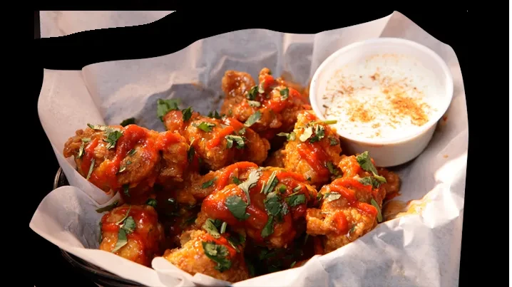 Crispy chicken bites in reddish-orange sauce, garnished with herbs and dip.