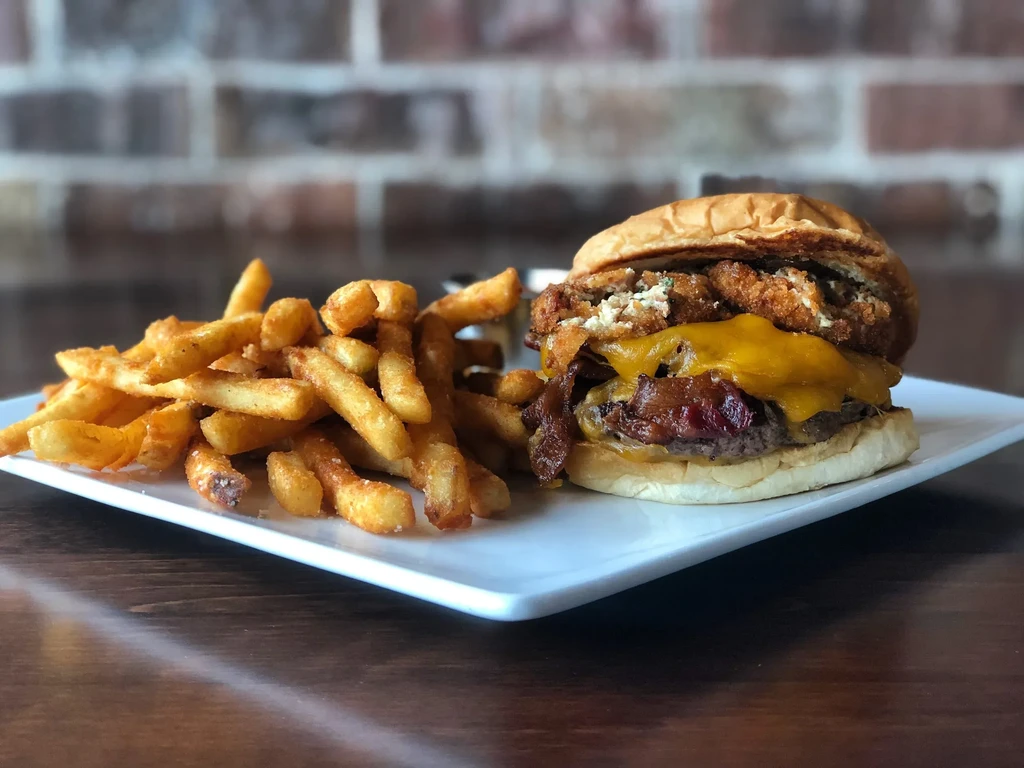 Close-up: Double-decker burger, melted cheese, bacon, and golden fries.
