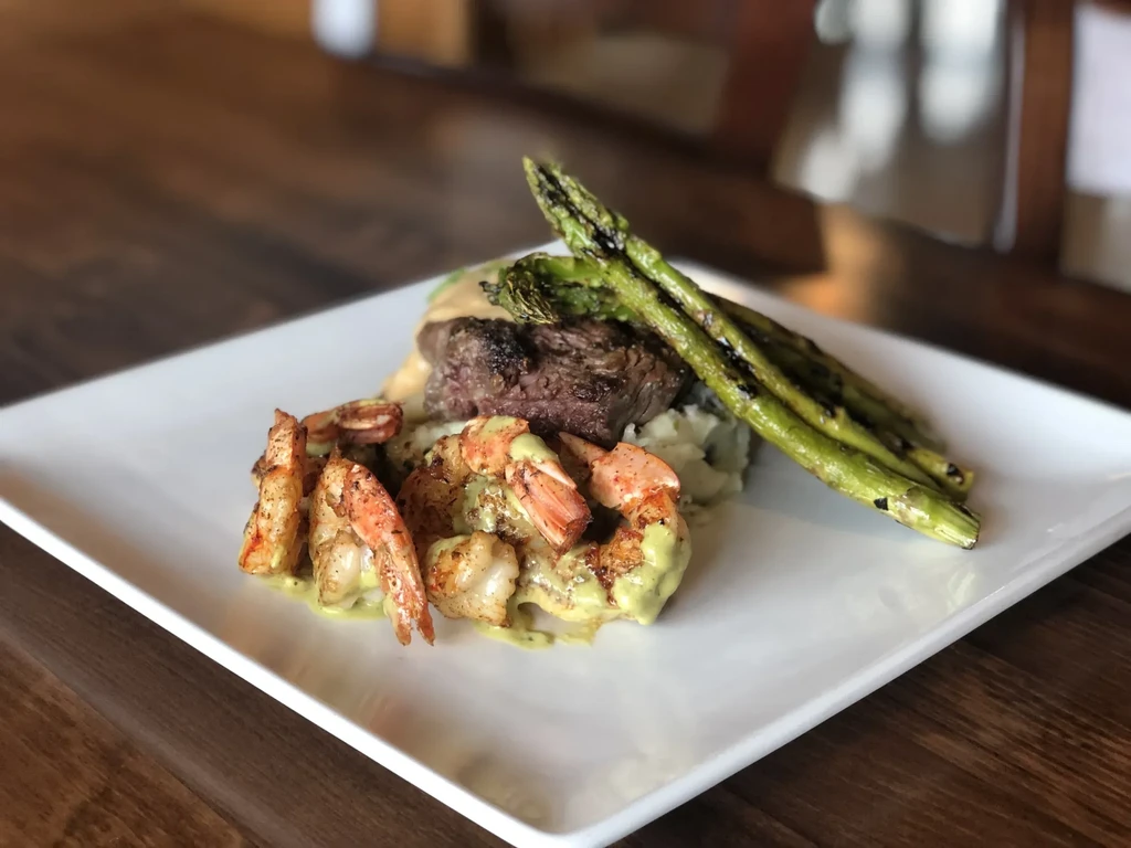 Medium-rare steak, shrimp, mashed potatoes, and asparagus plated.