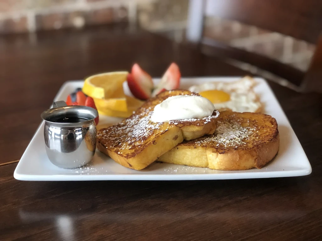 Two slices of French toast with whipped cream, powdered sugar, and fresh fruit.