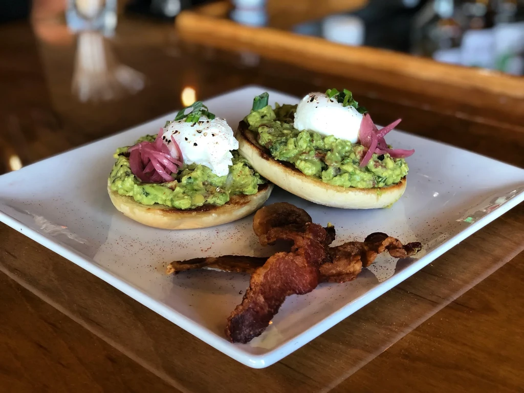 Plate of avocado English muffins, poached eggs, bacon, and pickled onions.