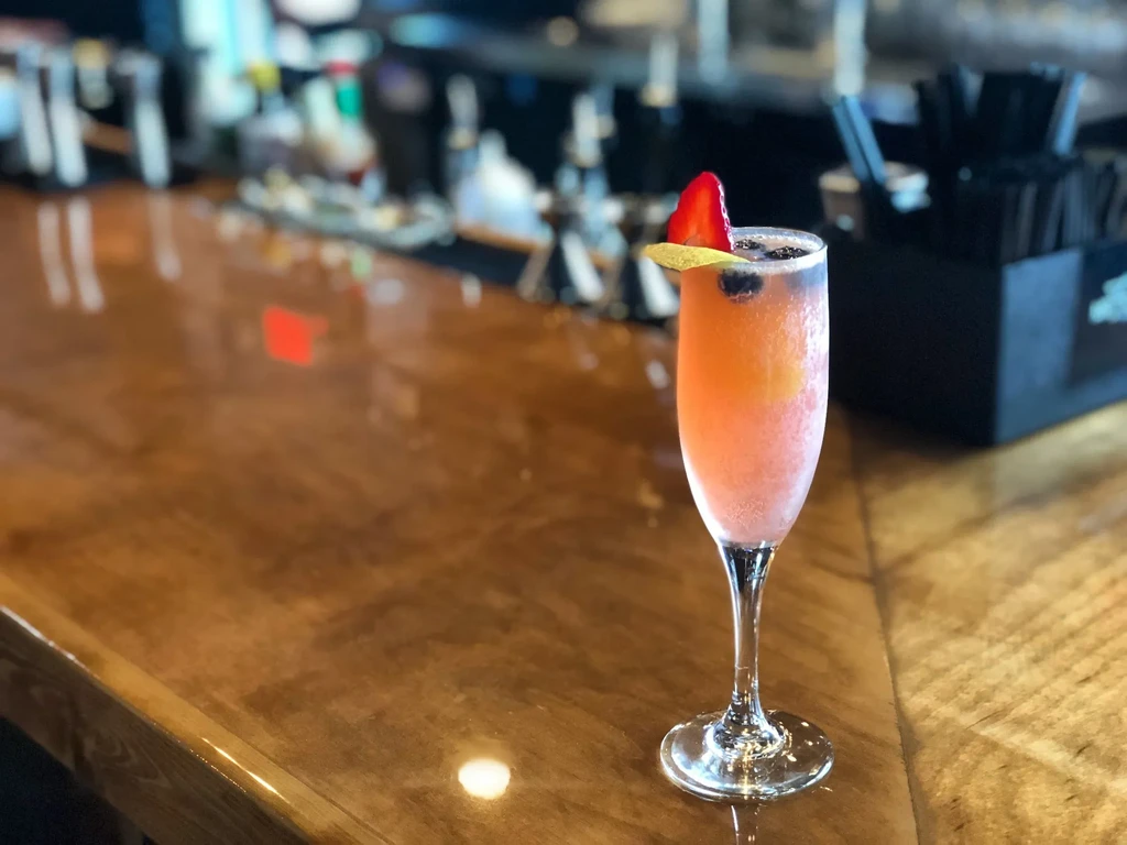 Effervescent pink and orange cocktail with fruit garnish on bar.