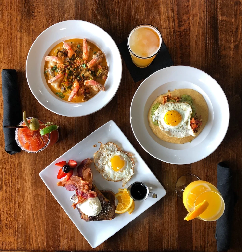 Overhead shot of wooden table with multiple brunch dishes and beverages.