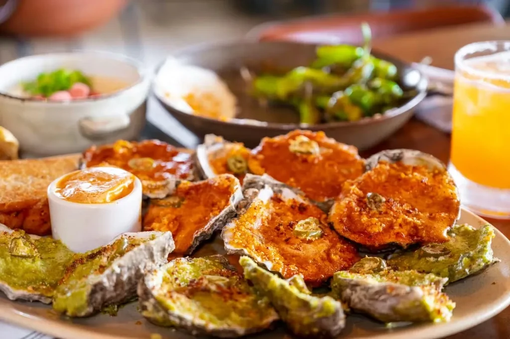 Oyster platter with colorful toppings, sauces, and drinks on a restaurant table.