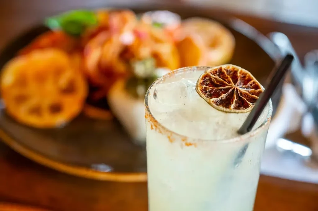 Margarita with chili-salt rim, dried citrus, black straw, blurred food.