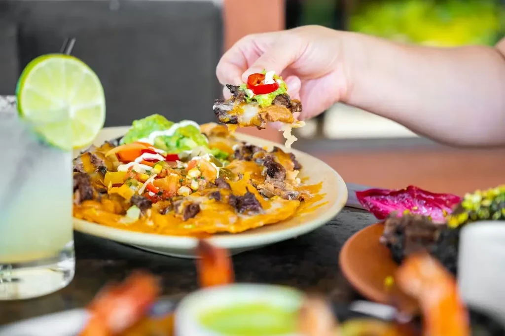 Hand pulls a cheesy nacho from a plate of loaded nachos.