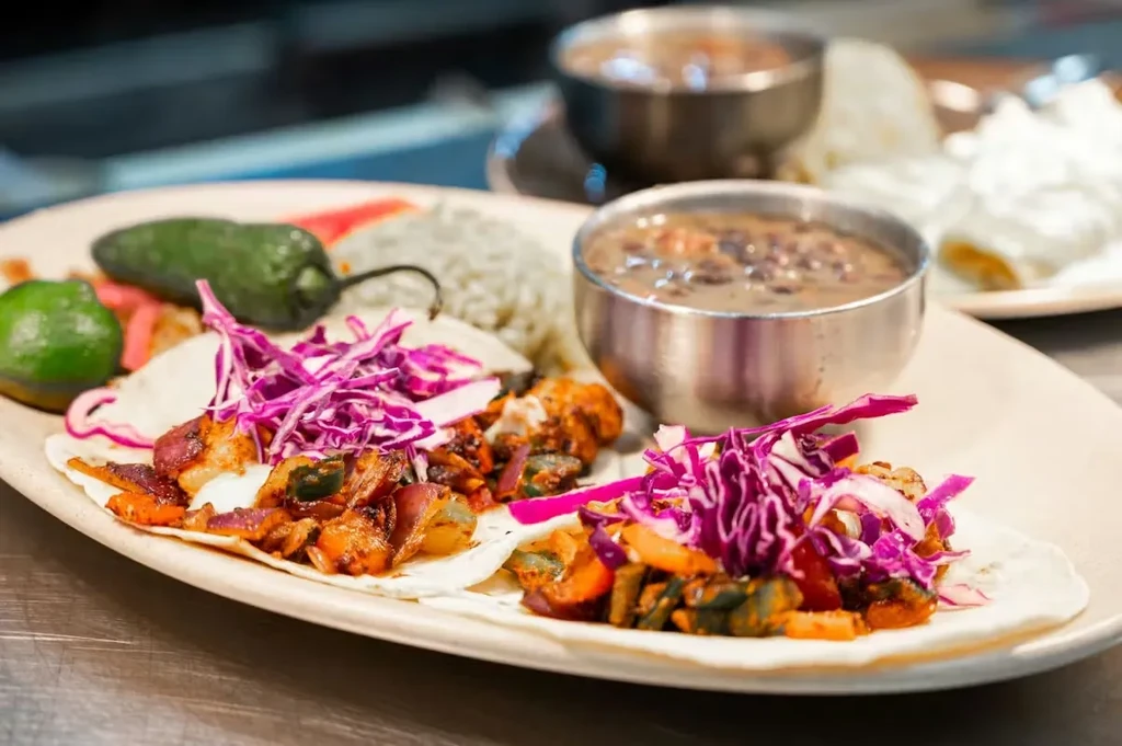 Close-up: Tacos topped with purple cabbage, rice, lime, chili, and stew.
