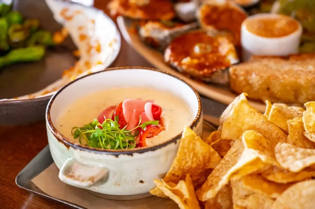 Creamy dip with red vegetables, microgreens, and crispy golden chips.