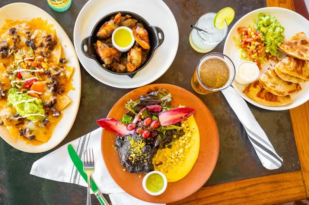 Overhead shot of nachos, quesadillas, a cocktail, beer, and other dishes.