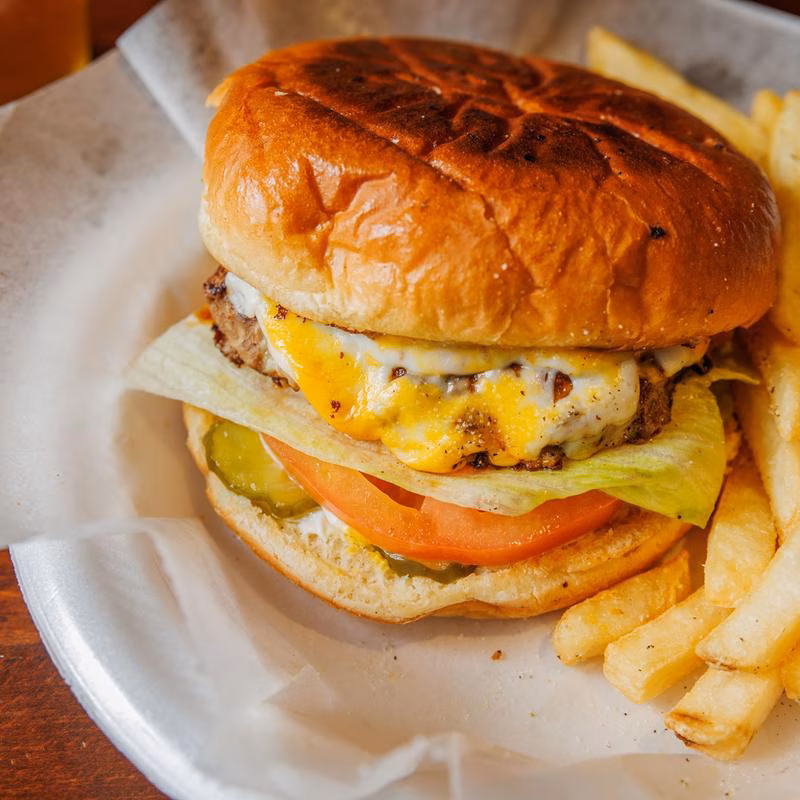 A cheeseburger with melted cheese, lettuce, tomato, pickles, and french fries.