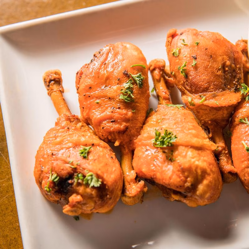 Cooked chicken drumsticks with herbs on a white rectangular plate.