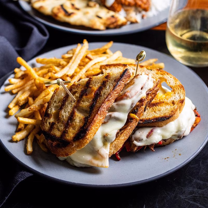 Plate of grilled sandwich with melted cheese and a side of fries.
