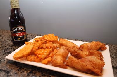 Fried battered fish, chips, and a bottle of malt vinegar.