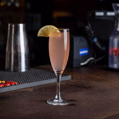 Pink drink in a champagne flute with lemon slice on bar.