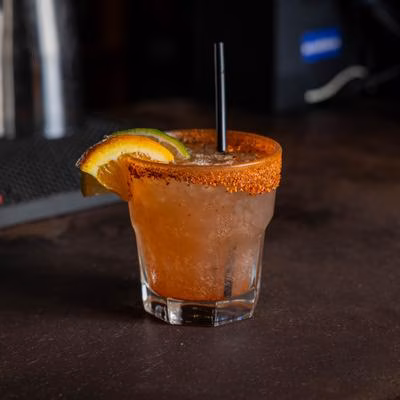 Cocktail in a glass with spiced rim, orange, lime, and black straw.