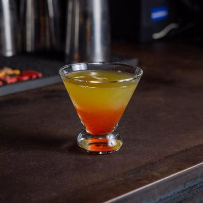 Colorful layered cocktail in a clear martini glass on a bar.