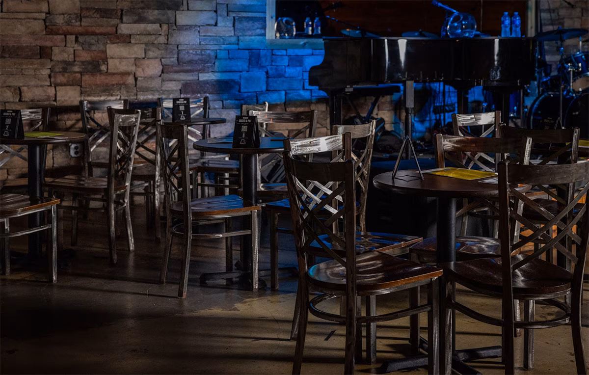 Dimly lit music venue with empty tables, chairs, and a stage.