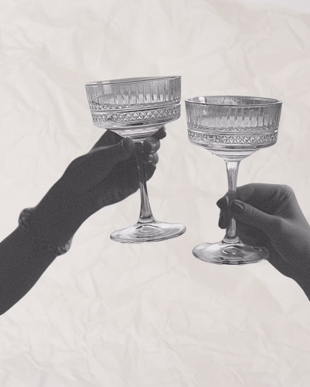 Two silhouetted hands clinking vintage coupe glasses against a crumpled background.