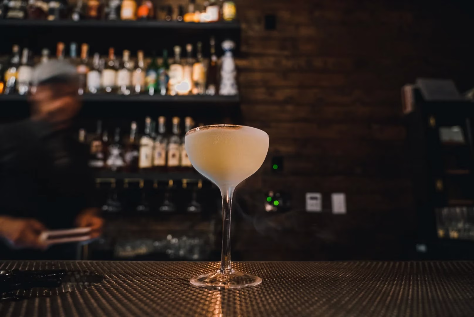 A frosted cocktail in a coupe glass on a dimly lit bar.