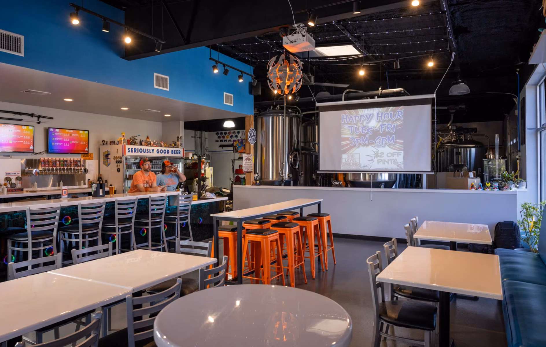 Interior of a modern brewery with a bar, tables, and brewing tanks.