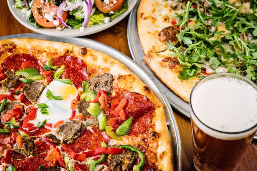 Pizza with egg, arugula pizza, salad, and a glass of beer.
