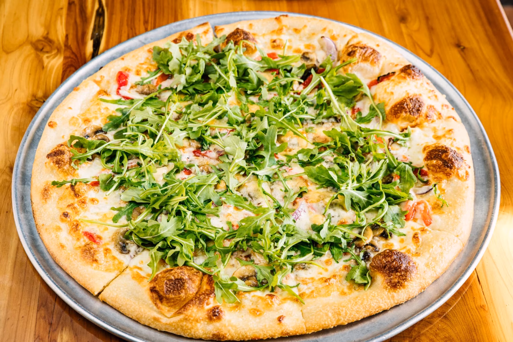 Whole pizza with arugula, mushrooms, red onions, and cheese.