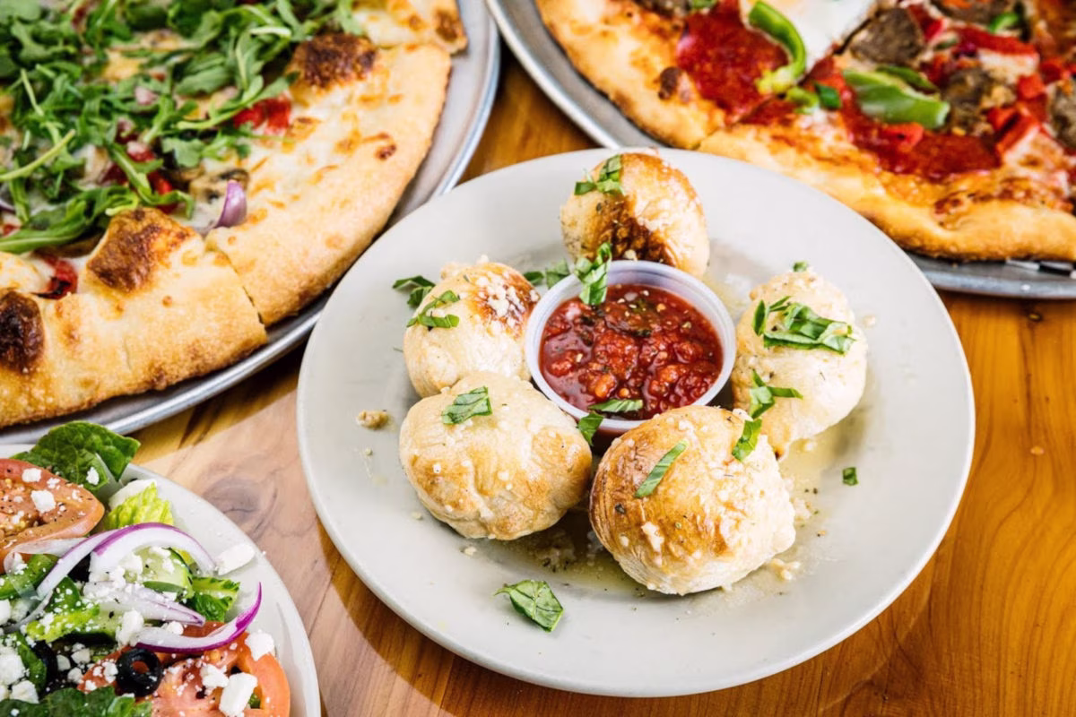 Garlic knots with marinara sauce, two pizzas, and a salad.