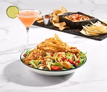 Fried chicken salad, pink cocktail, and tortilla chips with dip.