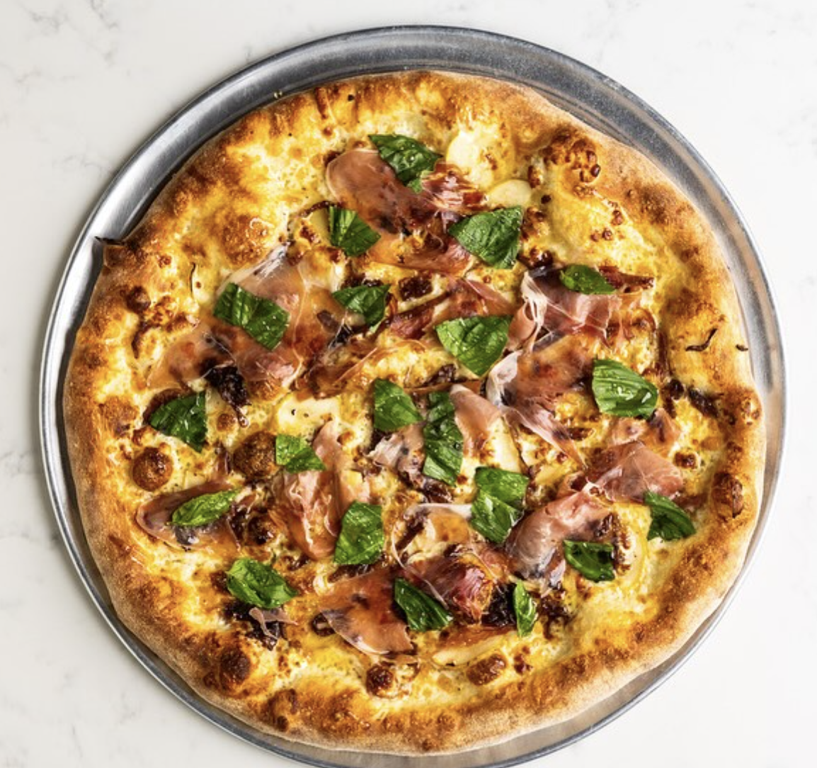 Pizza on a tray topped with prosciutto, cheese, and basil.