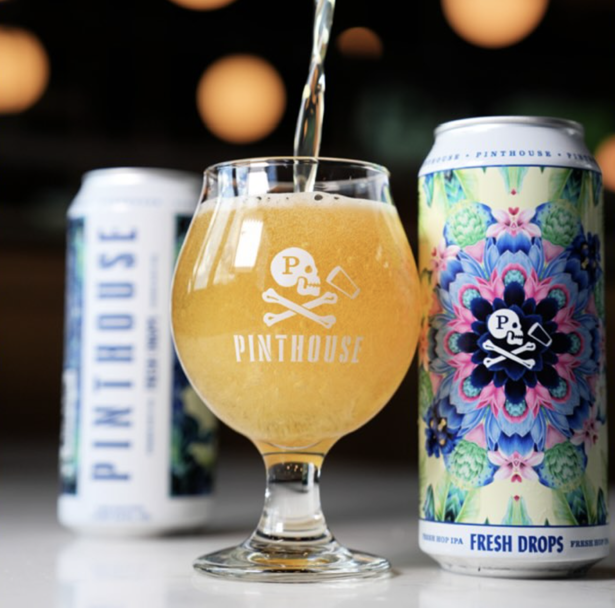 Pinthouse beer pouring into a branded glass, with two Pinthouse cans.