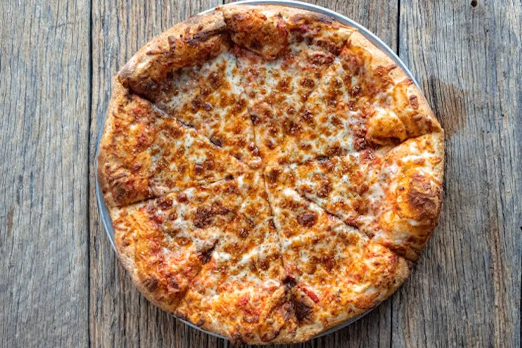 A whole cheese pizza, sliced, on a rustic wooden table.