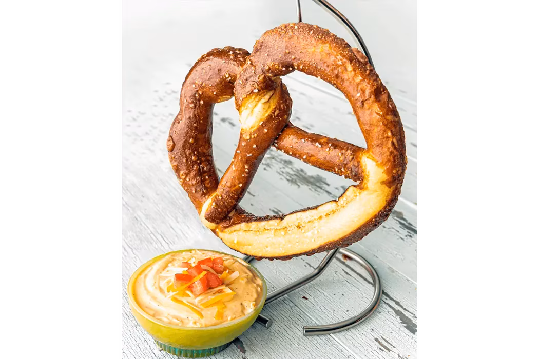 Salted pretzel on a stand with a bowl of cheese dip.