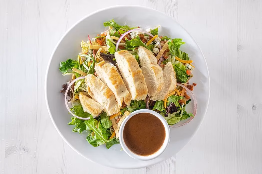 Grilled chicken salad with greens, cheese, onion, and dressing.