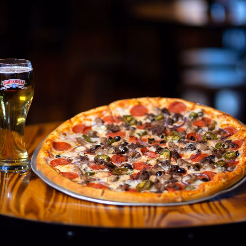 Pizza with pepperoni, vegetables, meat, and cheese next to beer.