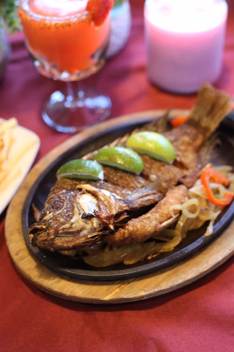 Fried whole fish with lime and onions on a black platter.