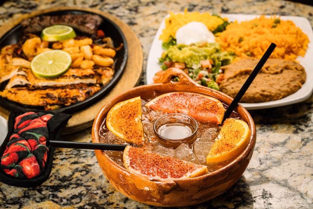 Sizzling fajitas, rice, beans, guacamole, and large citrus beverage.