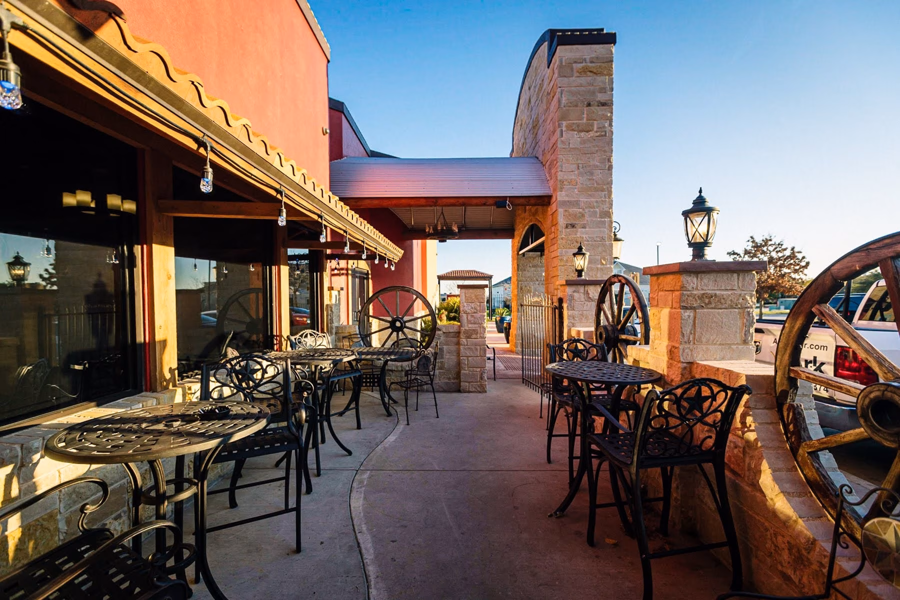 Outdoor patio with tables, chairs, and wagon wheels under sunset light.