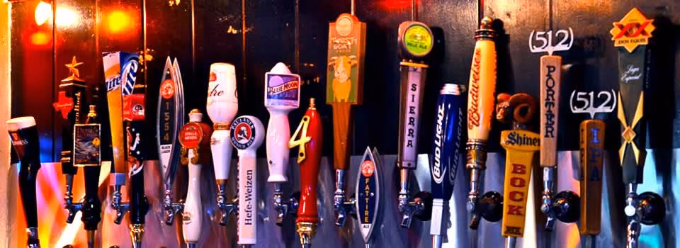 Numerous beer tap handles for different brands at a bar.