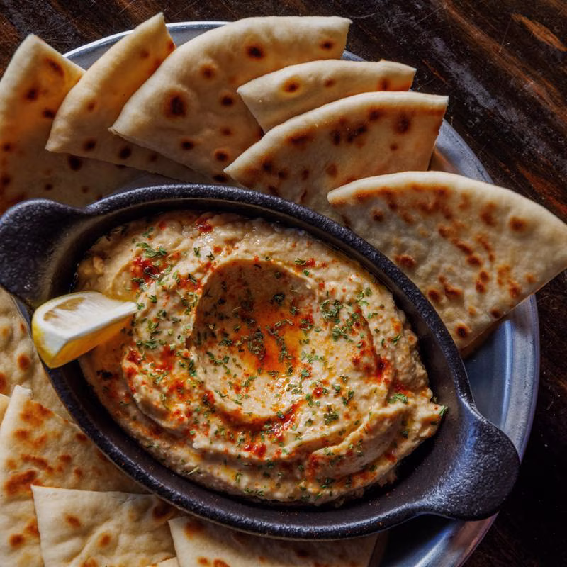 Hummus garnished with lemon and herbs, served with pita bread.