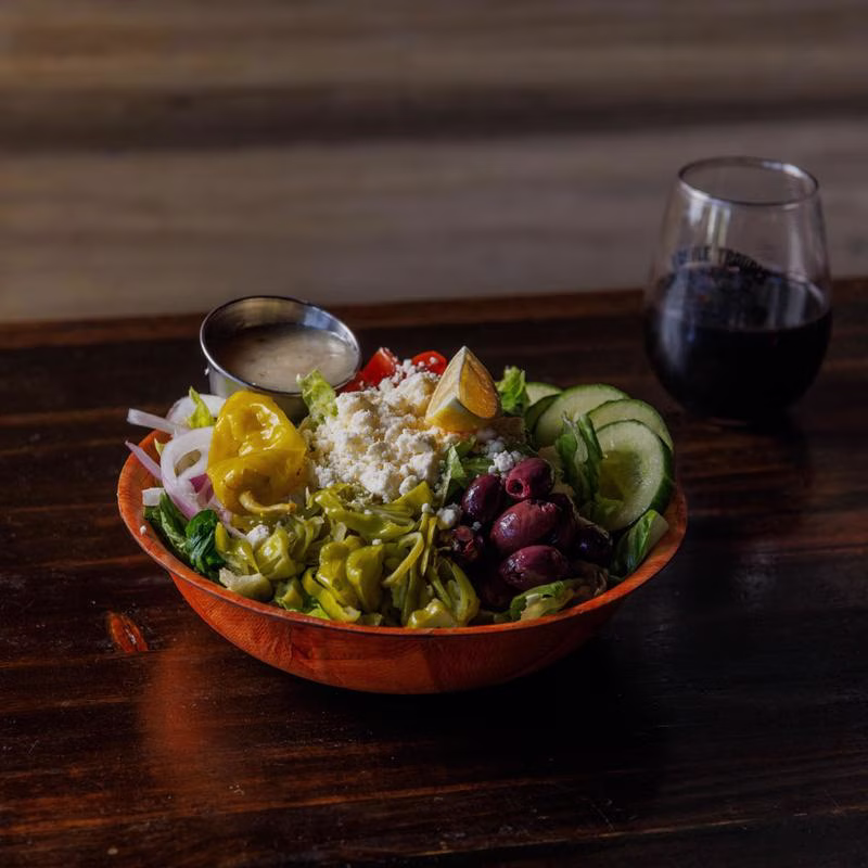A large Greek salad with dressing and a glass of red wine.