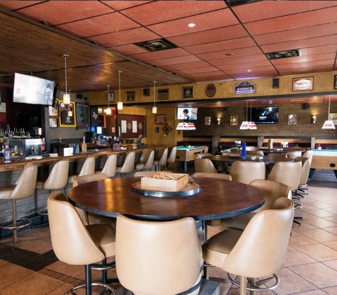 An empty bar with a long counter, high chairs, tables, and pool tables.