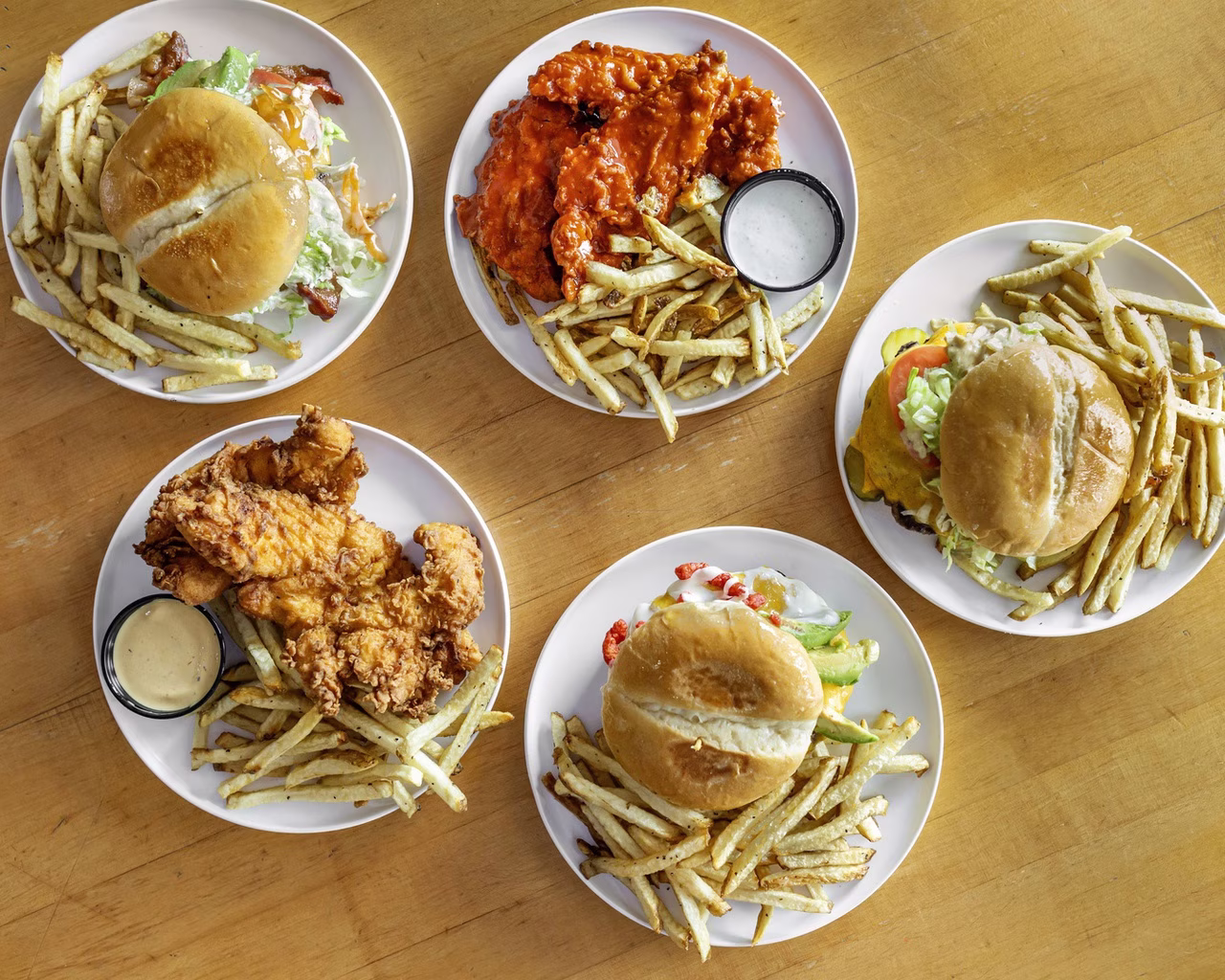Five plates with burgers, various chicken dishes, and french fries.