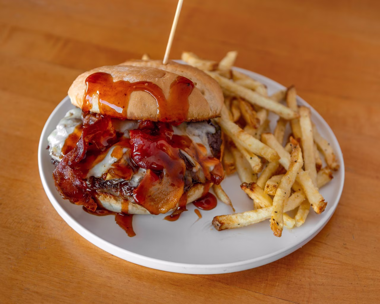 Burger with bacon, cheese, sauce, and fries on a white plate.