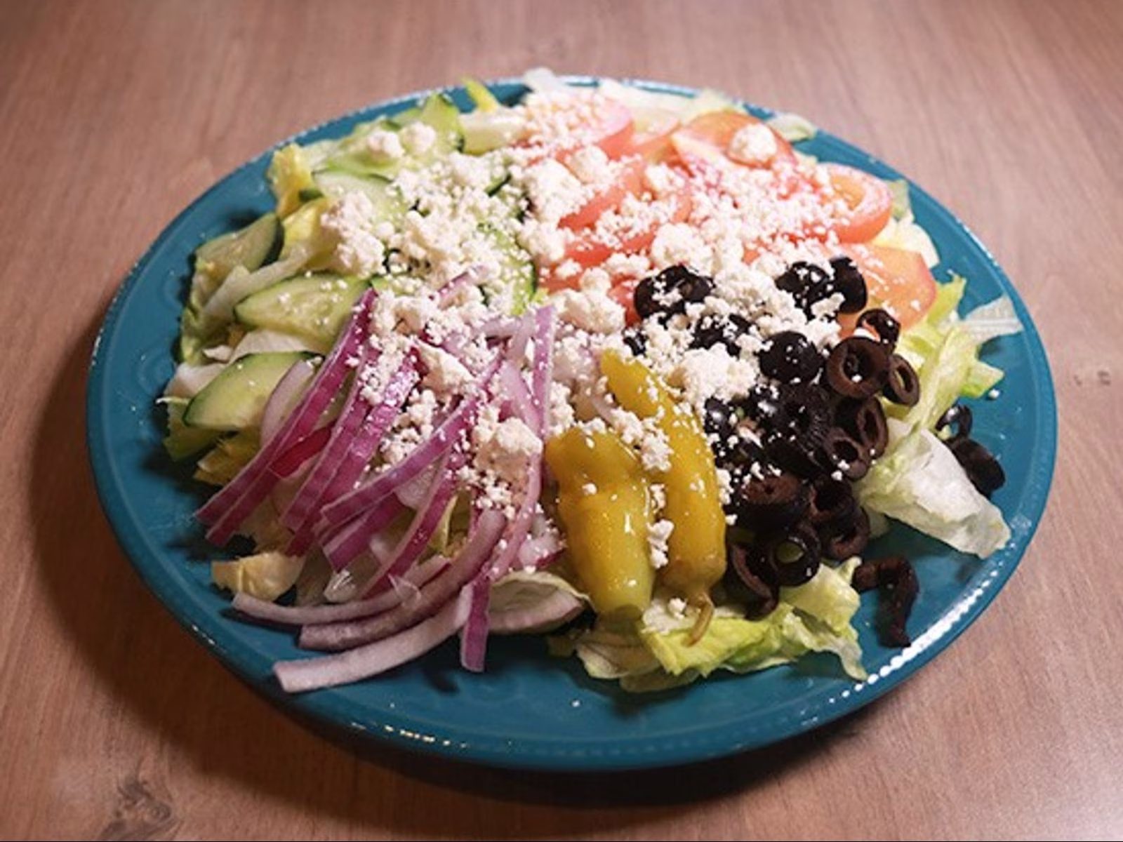 A salad with lettuce, cucumbers, tomatoes, feta, olives, onions, and peppers.