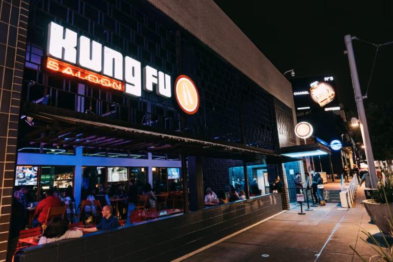 Exterior of Kung Fu Saloon at night with illuminated sign and patrons.