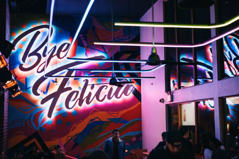 Colorful mural with "Bye Felicia" neon sign, purple and blue lighting.
