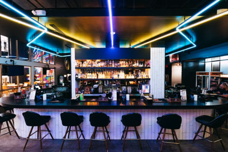 Modern bar with neon lights and shelves of liquor bottles.