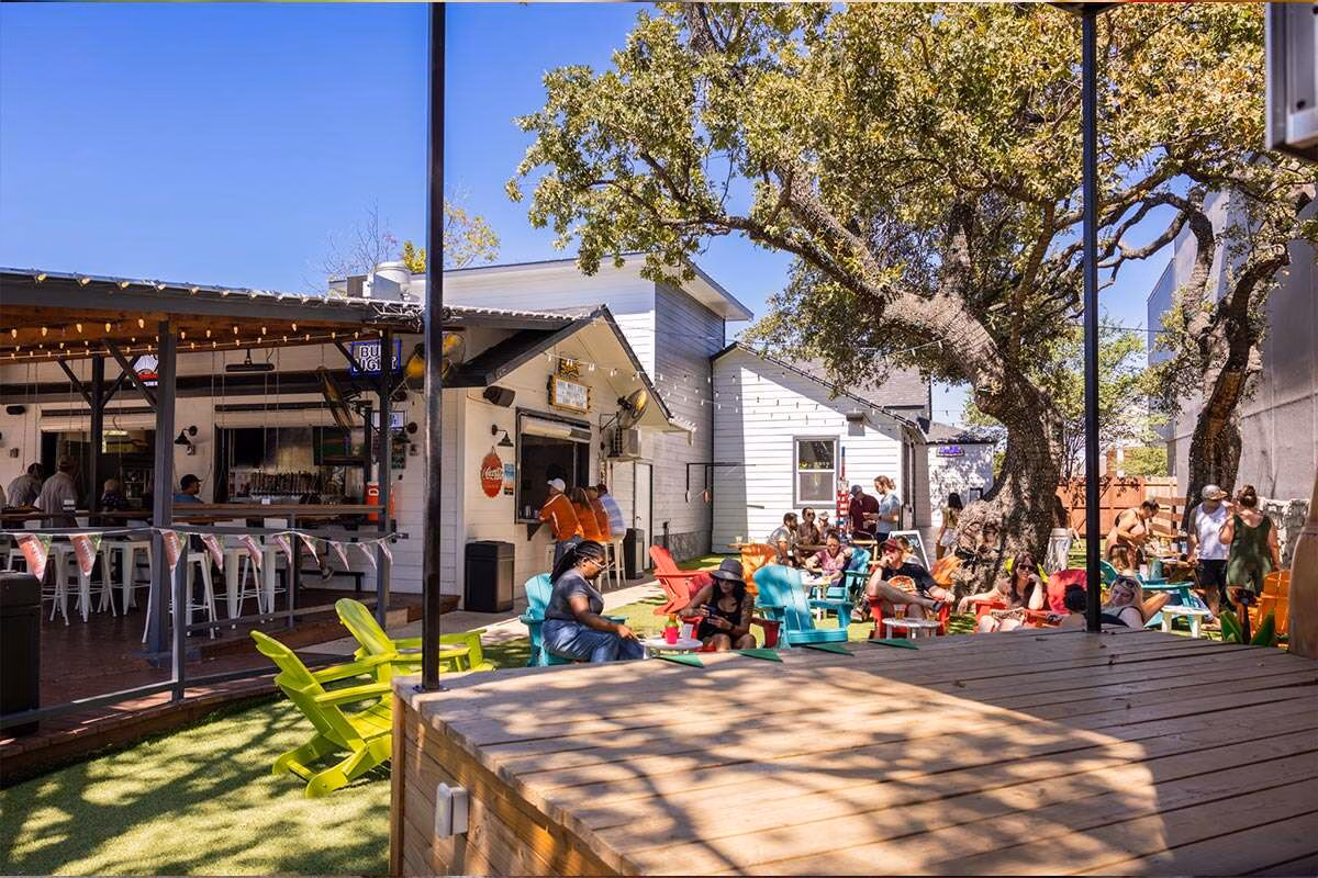 Outdoor bar and patio with people relaxing under large trees.