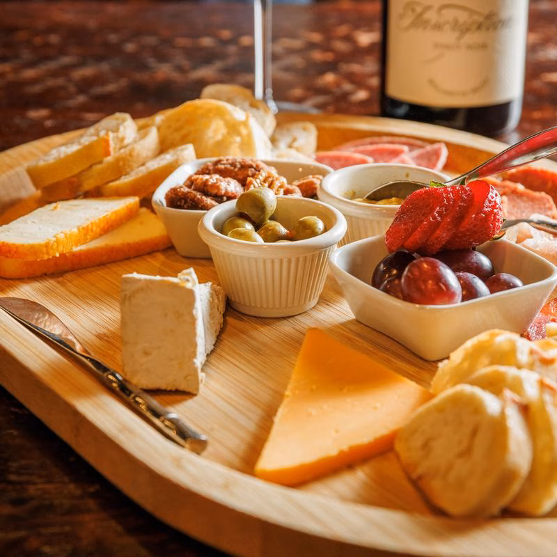 Wooden platter with various cheeses, bread, fruits, nuts, and olives.