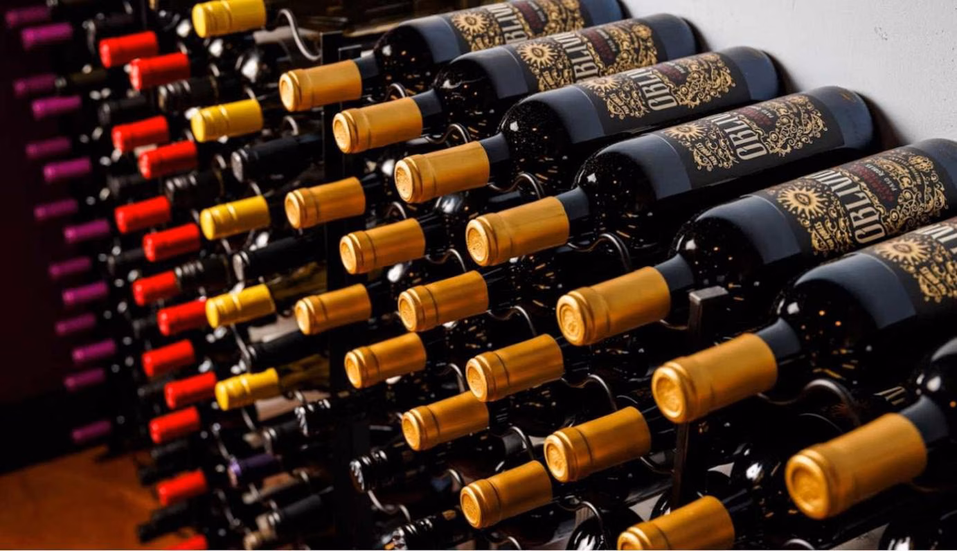 Rows of wine bottles with gold, red, and purple caps.